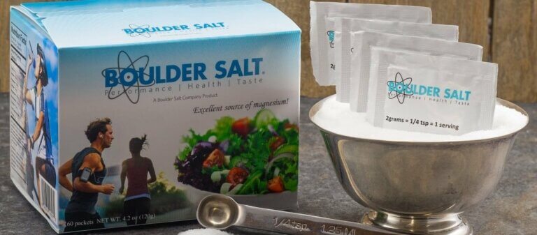 A box of Boulder Salt next to a bowl of salt with boulder salt packets on top