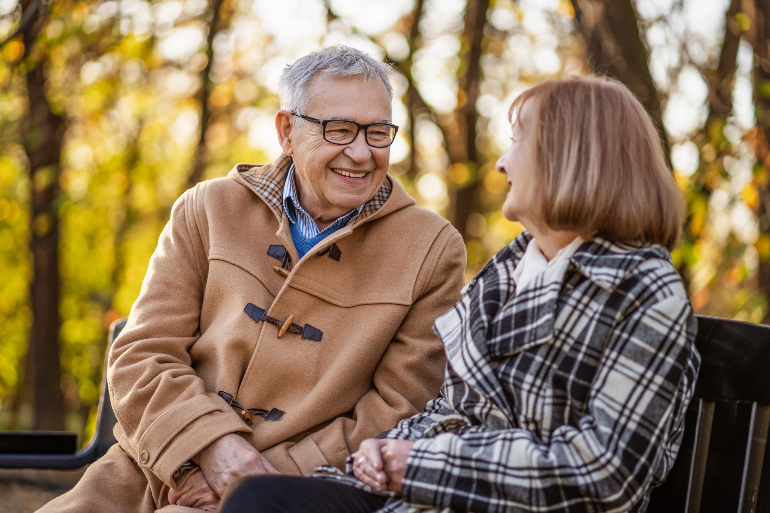 A happy senior couple sitting together on a park bench during a fall day, illustrating how Boulder Salt supports healthy blood pressure and vitality in every stage of life.